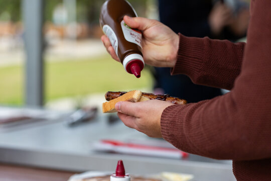 Man pouring barbecue sauce on sausage cooked on park BBQ