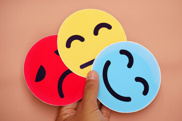 Hand holding three cards of frowning face, ambivalent face and smiling face. The concept of bipolar, mental health, depression, mood swings and multiple personalities.