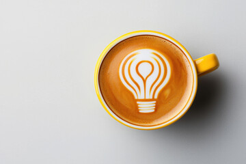 Creative coffee art in a yellow cup depicting a light bulb design.