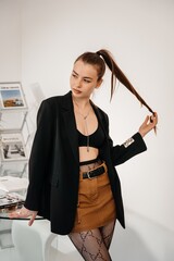 This photo shows a girl standing near a table looking into the frame and twirling her hair while posing. The photo is made in minimalism, which gives it a special atmosphere.