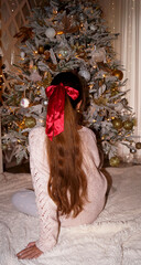 young girl with red ribbon in hair under the christmas tree