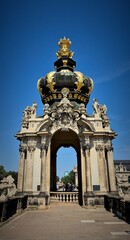 Obraz premium a dome on which rises a crown decorated with gold elements. The arch is surrounded by sculptures and decorative details such as stucco, bas-reliefs and columns. The background consists of a clear blue