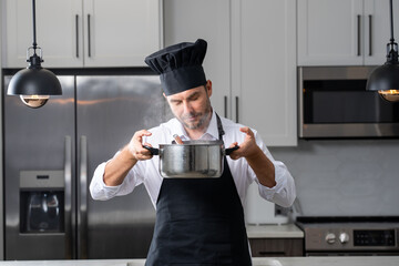 modern chef in professional uniform. close-up on the hand of male chef who is stirring soup in pot with spoon. cooking, culinary and people concept - male chef in toque with pot or saucepan.