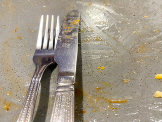 A knife and fork on a greasy plate at the end of a meal.