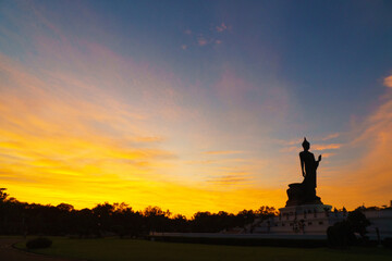 serene sunset view featuring large Buddha statue silhouetted against vibrant sky. warm colors of sunset create peaceful atmosphere