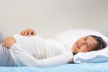 pregnant woman lying on bed, smiling and touching her belly, showcasing joy and anticipation. Soft lighting enhances serene atmosphere