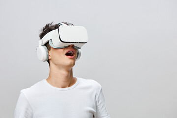 Young man experiencing virtual reality with a headset and headphones, bright background, engaged in...