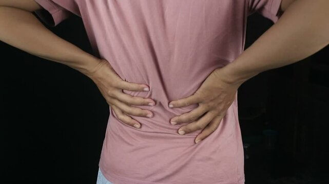 Rear view, man with back pain on black background, Close up hands touching back pain