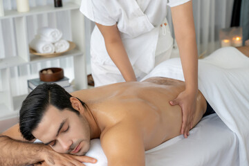 Fototapeta premium Caucasian man customer enjoying relaxing anti-stress spa massage and pampering with beauty skin recreation leisure in day light ambient salon spa at luxury resort or hotel. Quiescent
