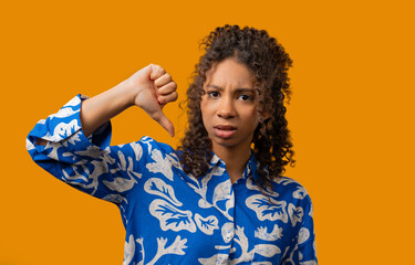 African teen girl with dislike sign. Stylish lady showing thumbs-down on yellow