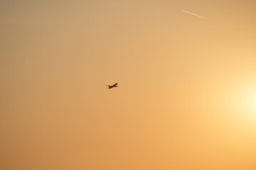 Fototapeta premium An airplane soars across the sunset sky, leaving a condensation trail in its wake. This image evokes a sense of freedom, travel, and adventure, capturing the beauty of air travel