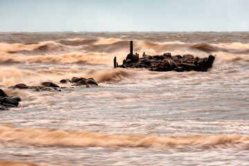 Naklejka premium dramatic storm in the Baltic Sea, large waves crashing against the stone pier, blurred, unclear contours, rocky shore of Vidzeme
