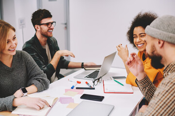 Positive male and female designers discussing creative ideas for developing startup project teamworking in office.Diversity group of cheerful hipsters students laughing during collaboration at desktop