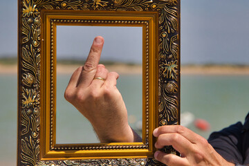 the finger of a man with a golden frame makes the gesture with the middle finger raised, expressing...
