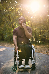 Fototapeta premium Man in Wheelchair Enjoying Nature While Using Phone Outdoors