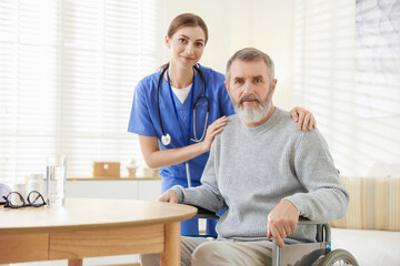 Caregiver assisting senior man in wheelchair indoors. Home health care service