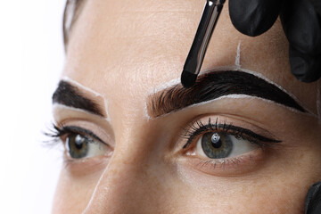 Young woman undergoing henna eyebrows dyeing on light background, closeup
