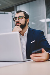 Thoughtful businessman dressed in suit thinking on productive strategy for developing own financial company working at modern laptop computer connected to wireless 4G internet in stylish office