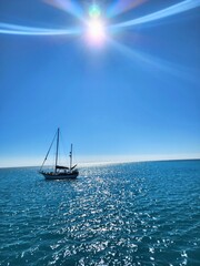 A sailboat gently cruising under the midday sun on sparkling blue waters, creating a serene marine scene.