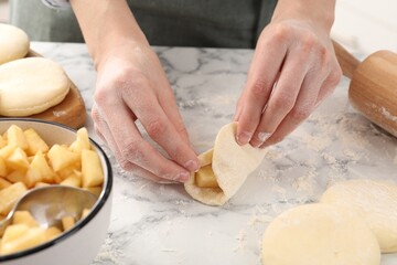 Woman making pirozhki (stuffed pastry pies) with apples at white marble table, closeup