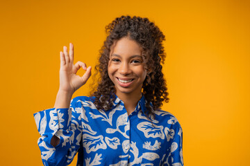 Positive teenager girl with hand sign Ok, Okay gesture.Lady on yellow studio