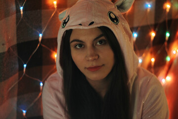 Woman in Unicorn Onesie Looking Pensive with Festive Lights Background