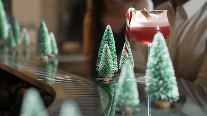 Focusing mixed punch cocktail christmas theme garnished with candy cane and cinnamon serving on luxury counter bar beside by green neon snow of Christmas tree special festive advertisement. Vinosity.