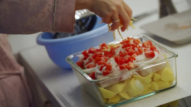 Woman cooking fish cod baked in oven with vegetables at home. Potatoes and cod fish fillet in oven baking dish with grated cheese. Healthy diet healthy food.