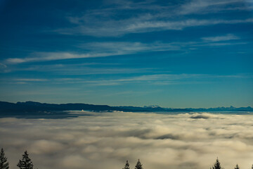 Aerial view of dense cloud inversion over valley floor with alpine mountains on far horizon.