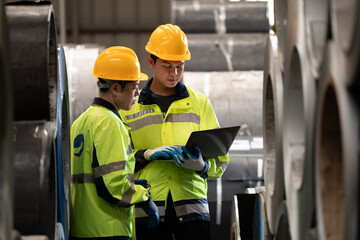 two professional engineer, worker, technician use clipboard discuss work, walk in steel metal manufacture factory plant industry.   Asian man and woman wear hard hat check quality machine.