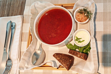 Traditional borscht served with fresh herbs, sour cream, and bread on a rustic table