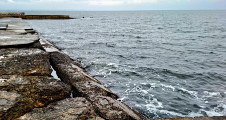 Fototapeta premium winter sea view. the dark blue waves of the Black Sea wash the stone slabs. winter. cloudy