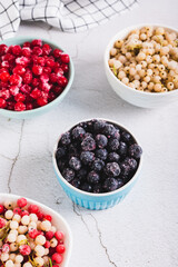 Frozen blackcurrants in a bowl and other berries on the table vertical view