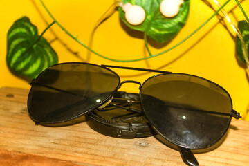 Sunglasses placed on a wooden block, decorated with leaves and a nightlight, on a bright yellow...