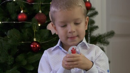 Happy child holding snow globe with figurine of Santa Claus. Smiling face of little boy near Christmas tree. Merry Christmas and Happy New year winter holidays.