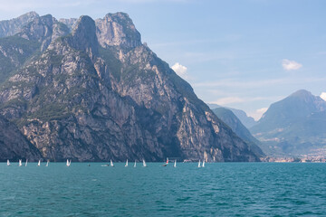 Small sailing boats floating on idyllic Lake Garda surrounded by steep rugged mountains of Garda Prealps. Looking from ferry boat near Nago-Torbole, Trentino, Italy. Peaceful summer travel destination