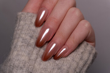 The nails of a woman’s hand in a gray sweater with a trendy Babyboomer manicure in soft pink-to-brown tones. The stylish manicure harmonizes perfectly with the light background.