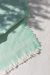 Green napkin or towel with fringe on white plaster background with leaves shadows. Copy space