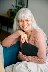 Obraz premium Smiling senior woman relaxing on sofa holding tablet at home