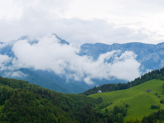 Fototapeta premium Mountain landscape with forest and clouds above it.