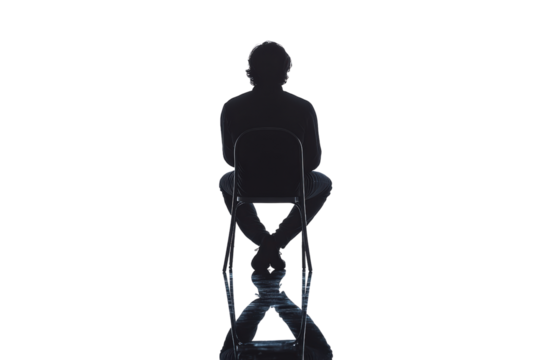 Silhouette of a person sitting on a chair, reflecting introspection and contemplation. The scene evokes a sense of solitude against a stark background.