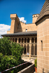 Fototapeta premium Long-haired blonde woman in a flowery dress looking out from one of the balconies of the impressive castle of Olite in Navarra on a sunny day
