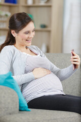 Obraz premium pregnant woman sitting on a couch taking a selfie