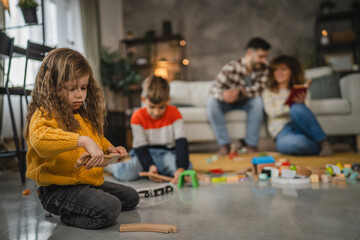 Obraz premium Parents and little children sit on floor and play with colorful toys