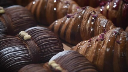 Close-up side view of fresh baked brown butterfly shaped croissants with hazelnuts lying on shelf of bakery or cafe by other puff pastry items. Handheld video. Copy space. Food background theme