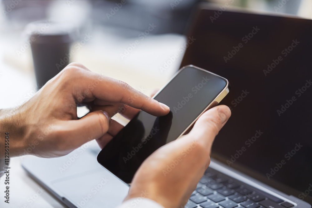 Poster focused image of a woman navigating her high-tech smartphone, laptop open next to her amidst the blu