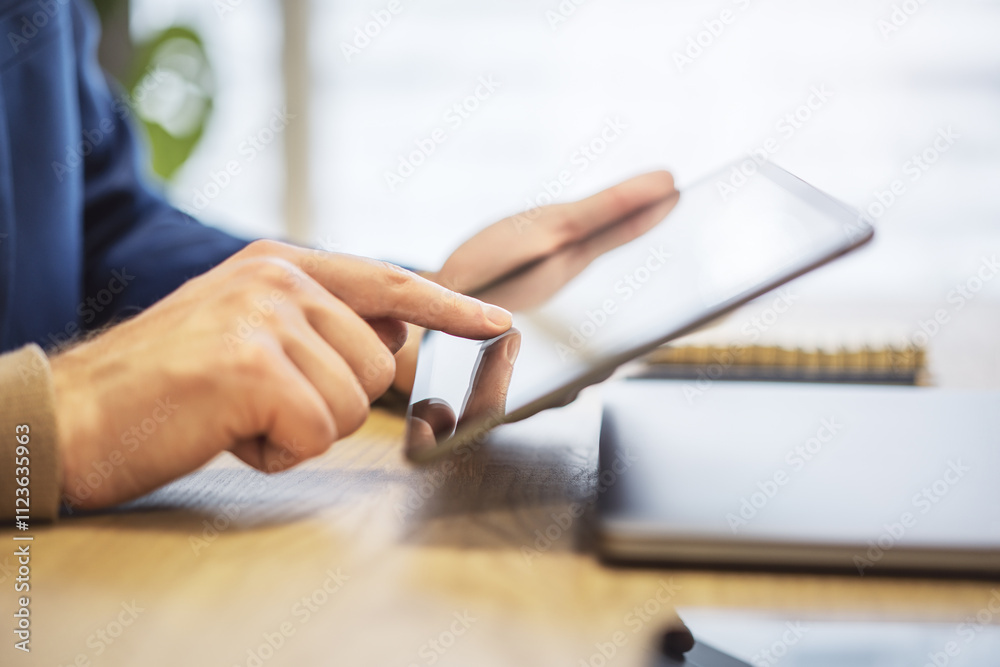 Poster closeup view of a male finger operating a high-tech tablet on a desk, set against the blurred backdr