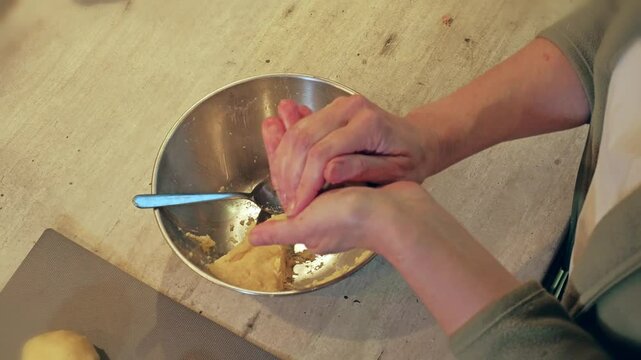 Closeup of housewife hands shaping traditional Polish Meat-filled potato dumplings called Pyzy with homemade dough In domestic kitchen setting