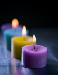 Row of colorful burning candles on dark backdrop.