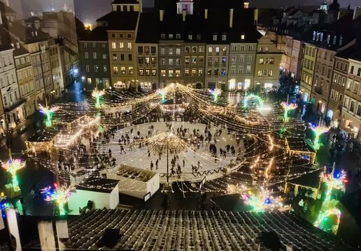 Świąteczny jarmark na starym mieście, wiecz&oacute;r, noc, kolorowe światełka, bożonarodzeniowa dekoracja, zimowa ślizgawka na rynku, ludzie jeżdżą na łyżwach, wesoła, świąteczna atmosfera.
